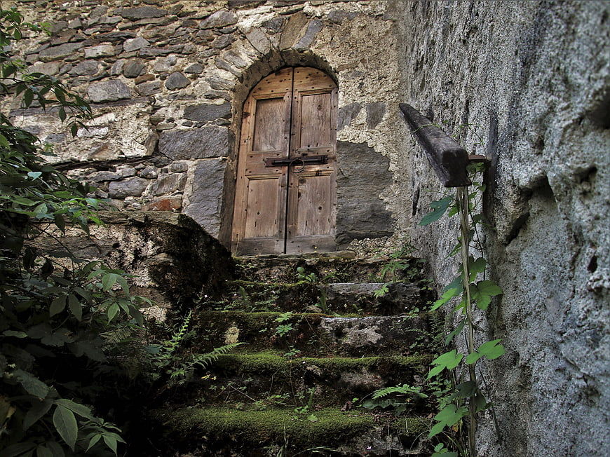 Mossy Stone Steps Leading To Weathered Wooden Door In Old Stone Wall