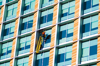 Window cleaner suspended on modern office building facade