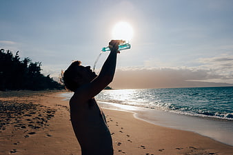 Man drinking water from bottle on tropical beach at sunset