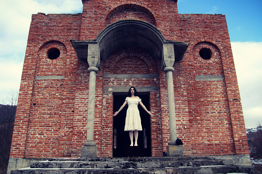 Woman in white dress floating in front of old brick church