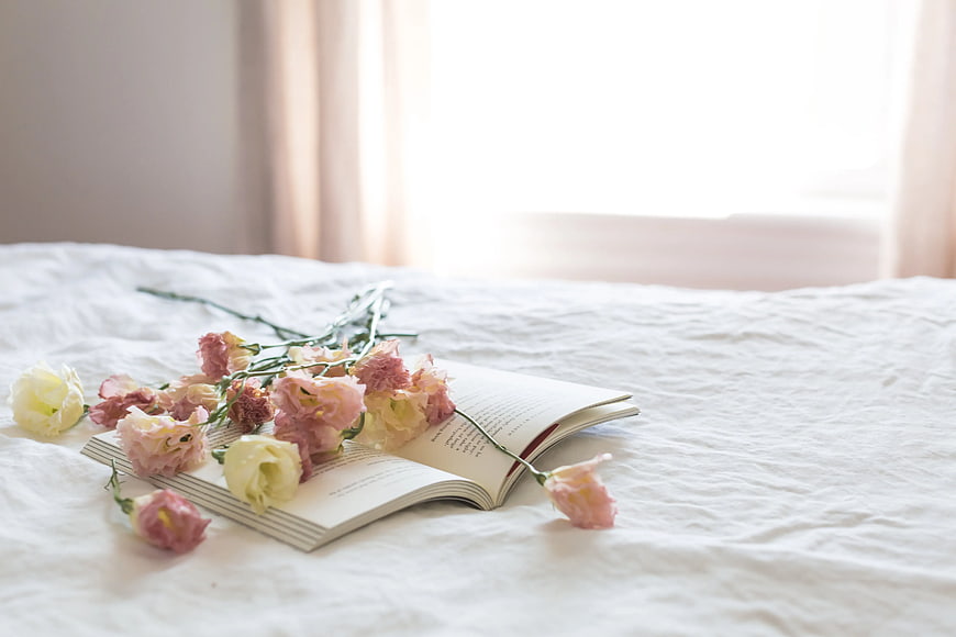 Pink flowers and open book on white bed linen