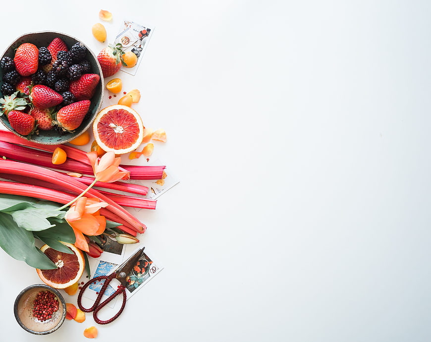 Flat lay of fresh berries, rhubarb, and flowers on white background