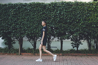 Woman in Black Dress Walking Past Green Hedge