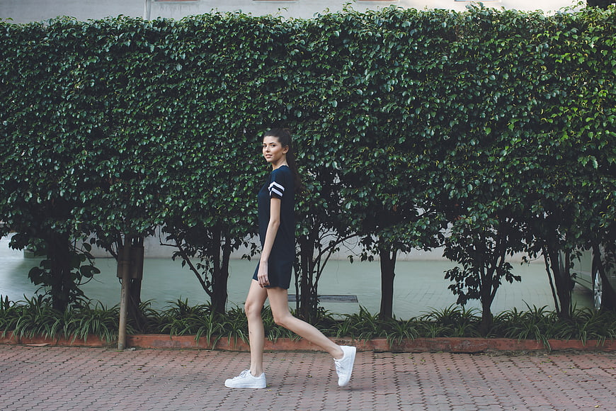 Woman in Black Dress Walking Past Green Hedge