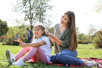 Mother braiding daughter's hair in sunny park