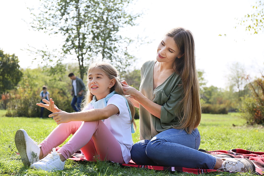Mother braiding daughter's hair in sunny park