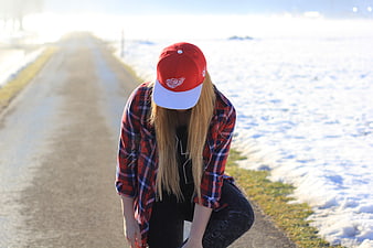 Woman in Red Cap and Plaid Shirt Crouching on Snowy Road