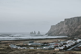 Village near dramatic cliffs and sea stacks on overcast day
