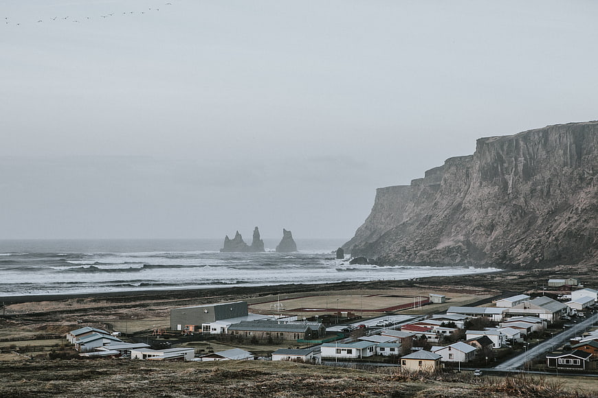 Village near dramatic cliffs and sea stacks on overcast day