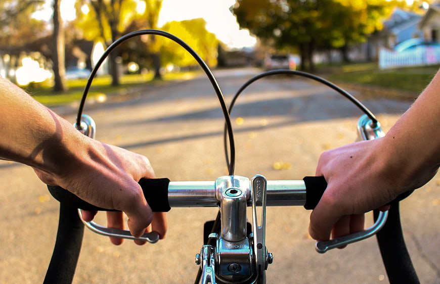 First Person View of Hands on Bicycle Handlebars in Autumn