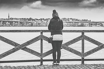Woman standing at wooden railing overlooking river and city skyline