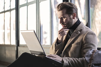 Thoughtful Bearded Man Working on Laptop by Window