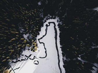 Aerial view of frozen lake surrounded by dark pine forest