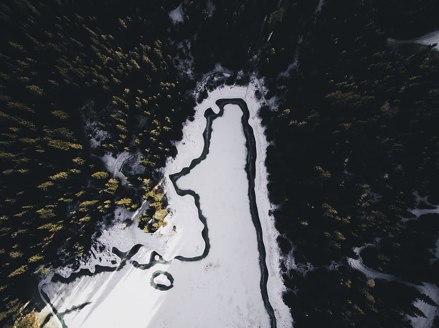 Aerial view of frozen lake surrounded by dark pine forest