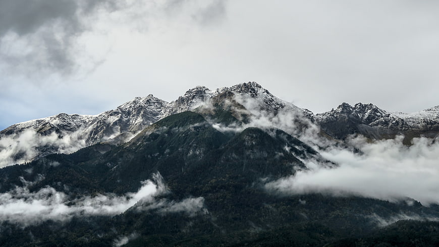 Snow-capped mountain peaks rising above swirling clouds and fog