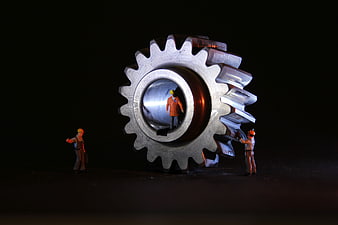 Miniature construction workers repairing a large metal gear