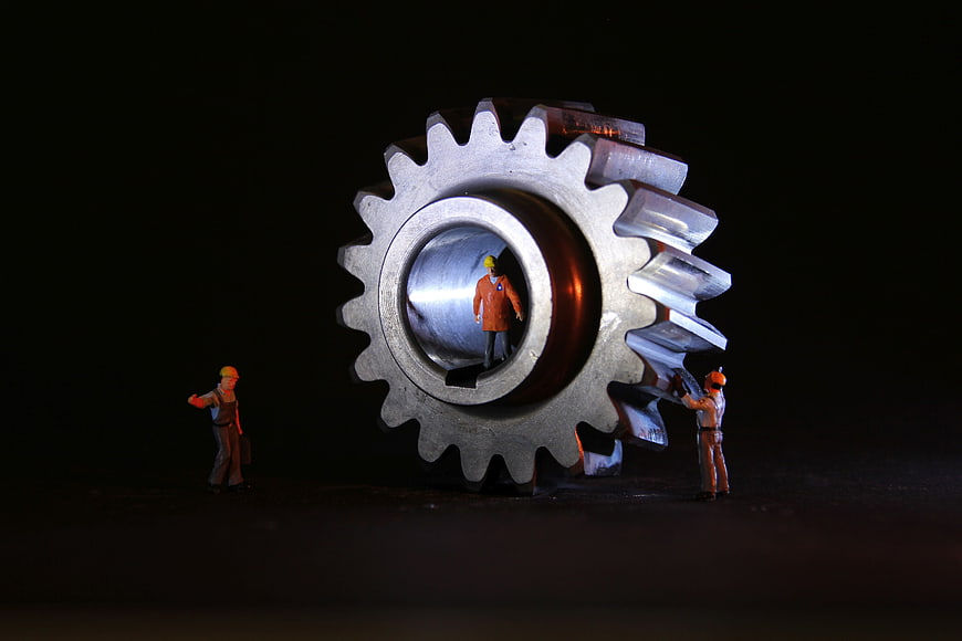 Miniature construction workers repairing a large metal gear