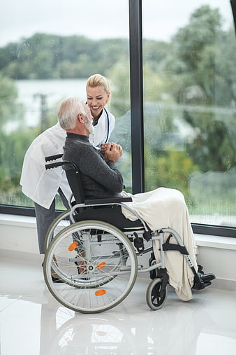 Female doctor comforting senior man in wheelchair by window
