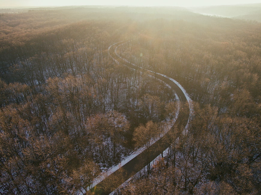 Aerial View of Winding Road Through Snowy Winter Forest