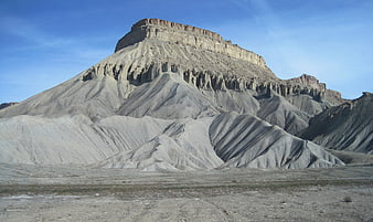 Dramatic desert mesa landscape with eroded slopes and blue sky