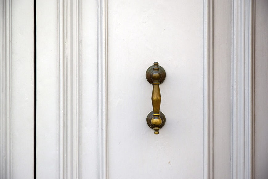 Close-up of vintage brass door handle on white paneled door