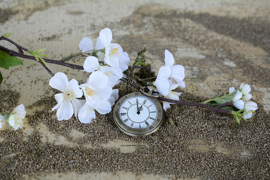 Vintage pocket watch with white flowers on sand and map