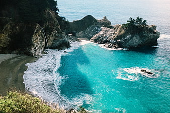 Aerial View of Secluded Turquoise Cove with Waterfall and Rocky Cliffs