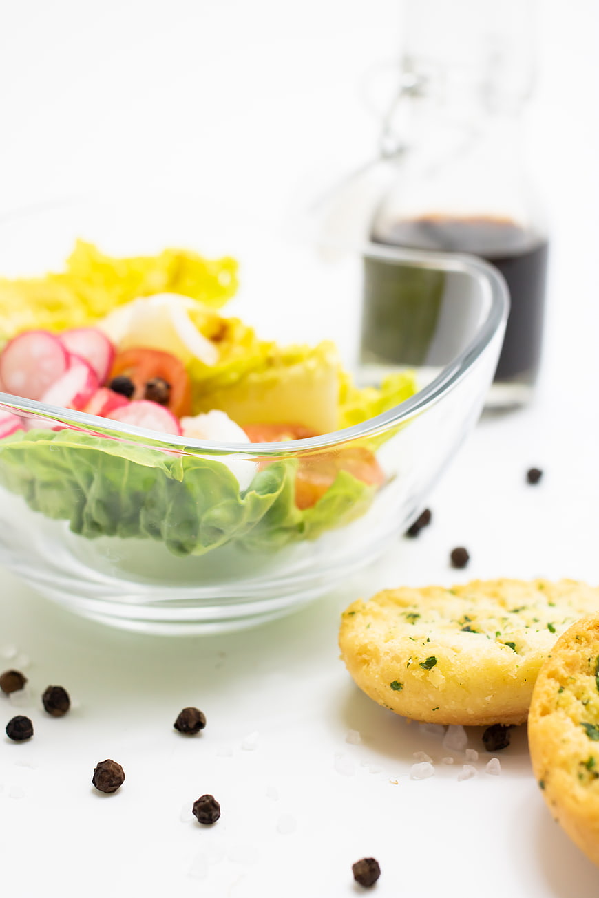 Fresh salad bowl with radishes and garlic bread on white background
