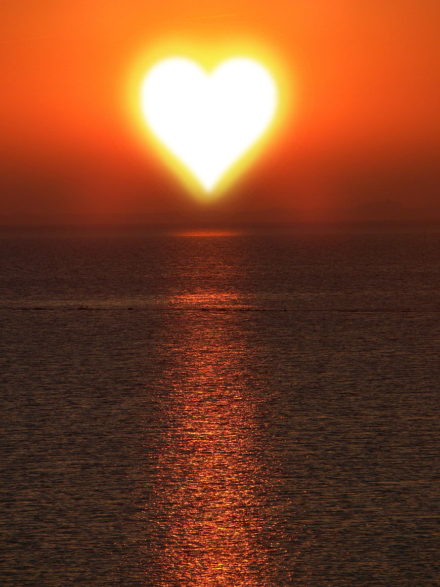 Heart-shaped sunset over ocean with golden reflection