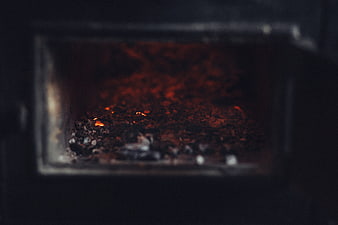Glowing embers and ashes inside a dark wood stove