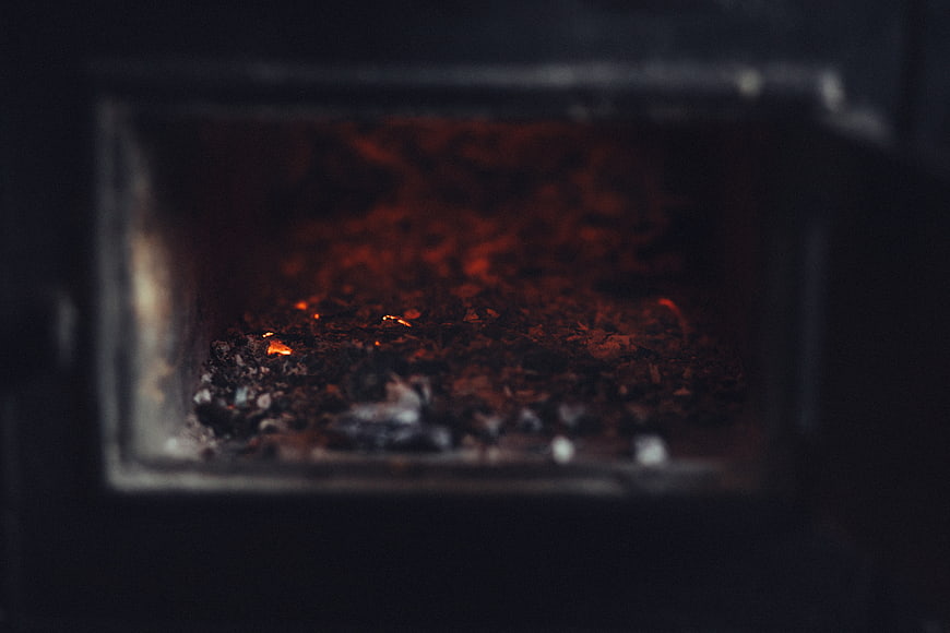 Glowing embers and ashes inside a dark wood stove