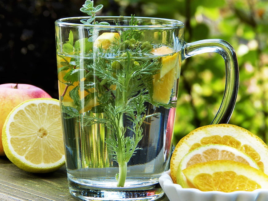 Glass mug of herbal tea with lemon, orange, and fresh herbs on a wooden table