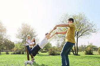 Happy family playing with dog in sunny park