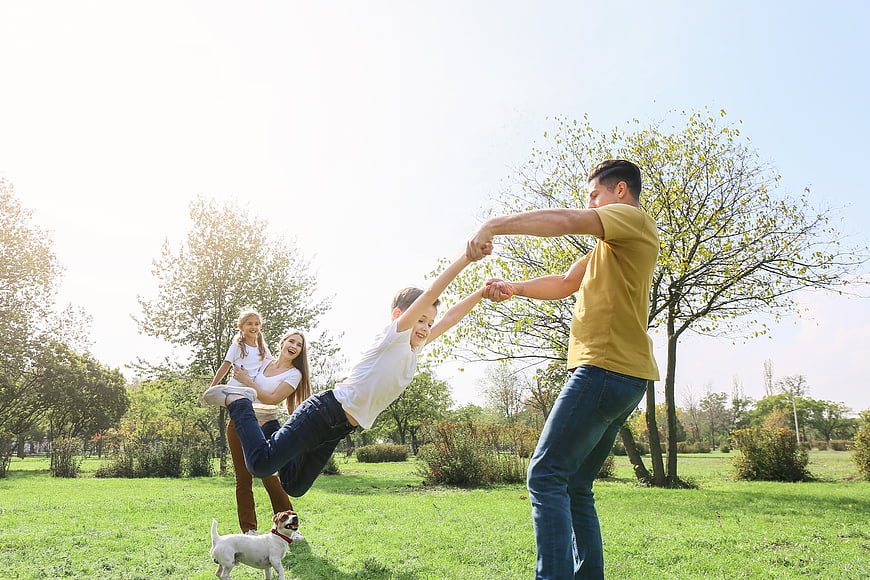 Happy family playing with dog in sunny park