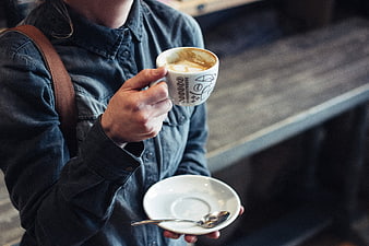 Woman holding cappuccino cup in denim jacket