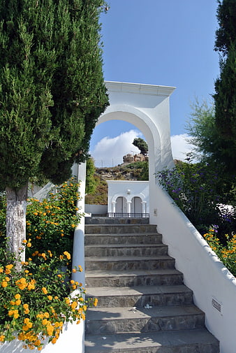 White arched gateway with stone steps and yellow flowers