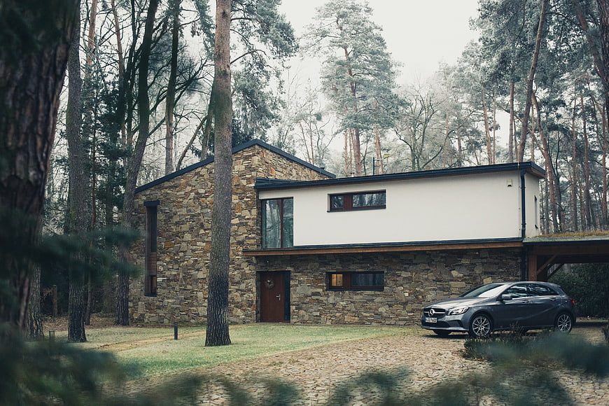 Modern stone house in pine forest with parked car
