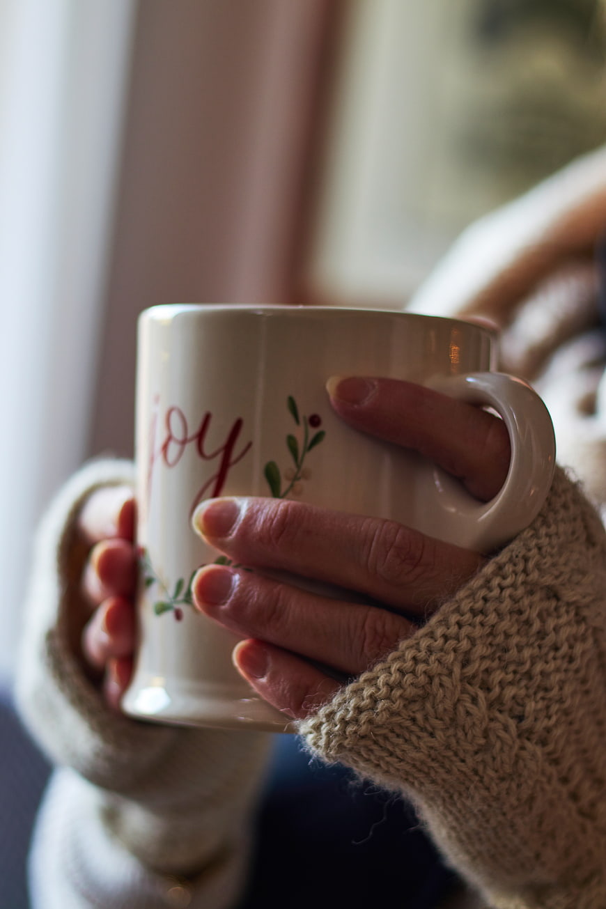 Cozy hands holding festive joy mug in winter sweater