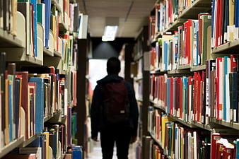 Student with backpack walking down library aisle