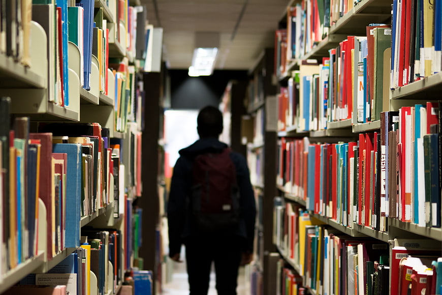 Student with backpack walking down library aisle