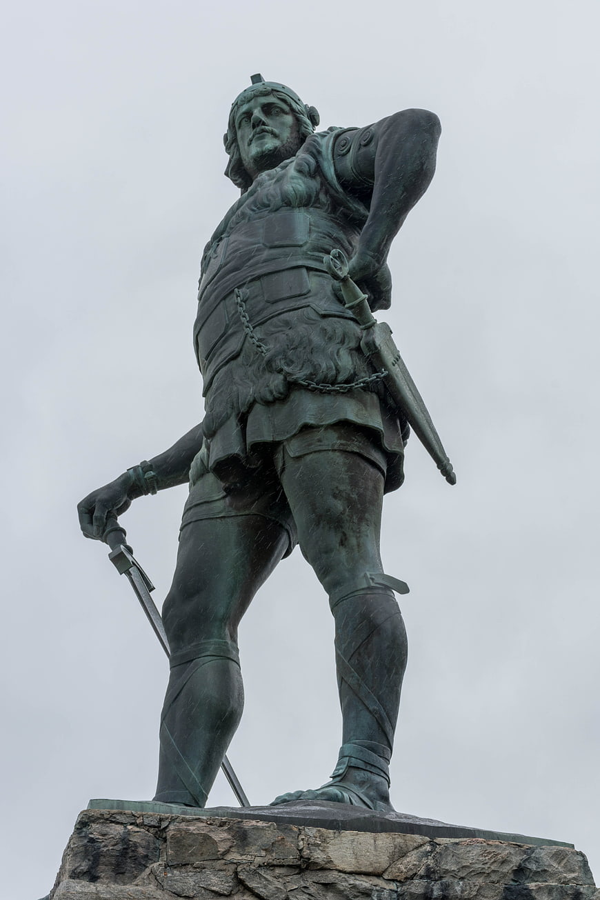 Low angle view of bronze warrior statue on stone pedestal