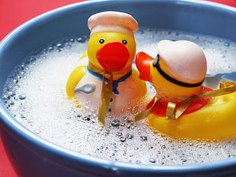 Two rubber ducks in a blue bowl with soapy bubbles