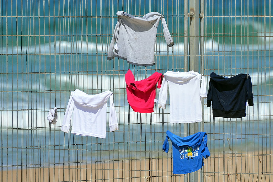 Children's clothing hanging on a beach fence with ocean waves in background