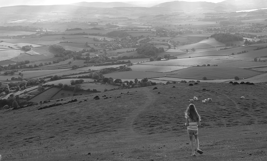 Woman walking on hillside overlooking rural valley landscape