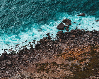 Aerial view of turquoise ocean waves crashing on rocky shore