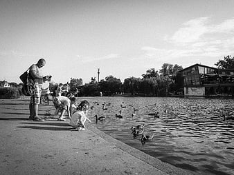 Black and white photo of family feeding ducks by lake