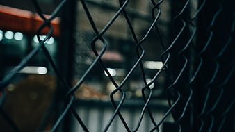 Close-up of dark chain-link fence with blurred city lights