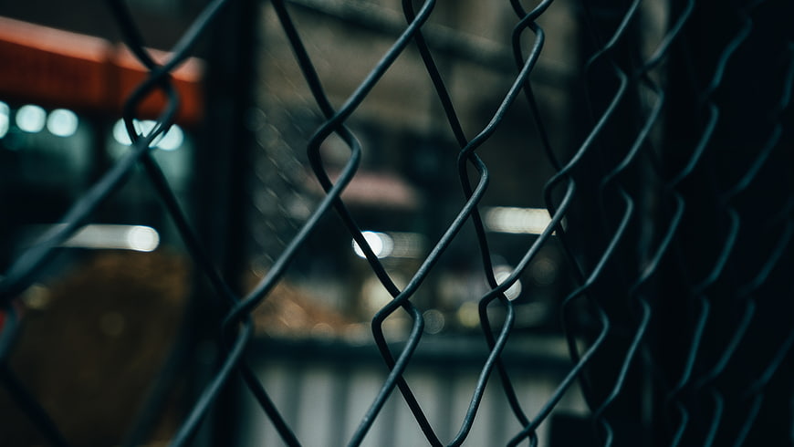 Close-up of dark chain-link fence with blurred city lights
