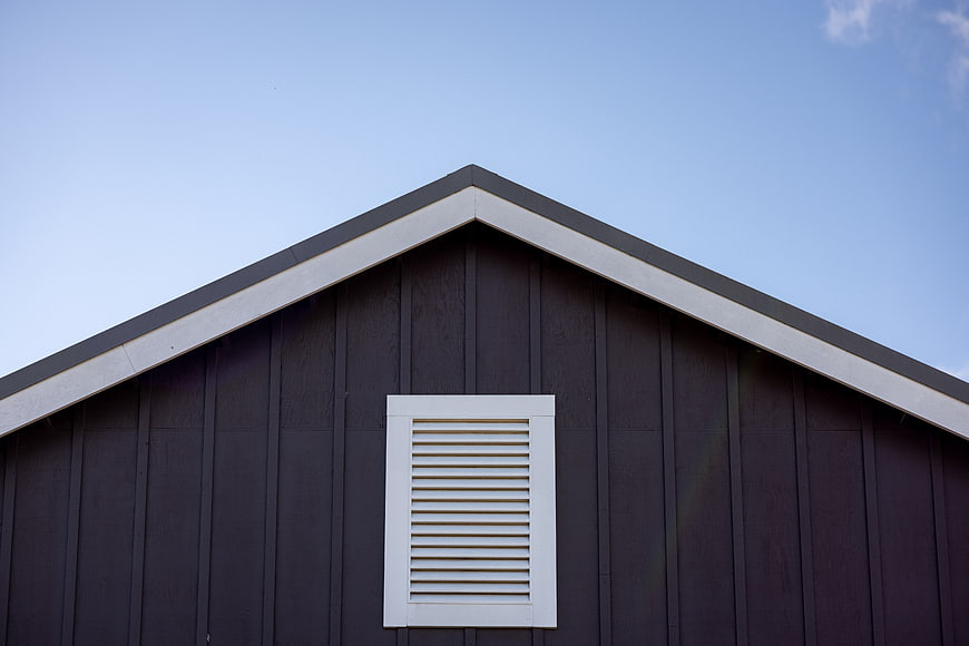 Minimalist black barn gable with white vent against blue sky