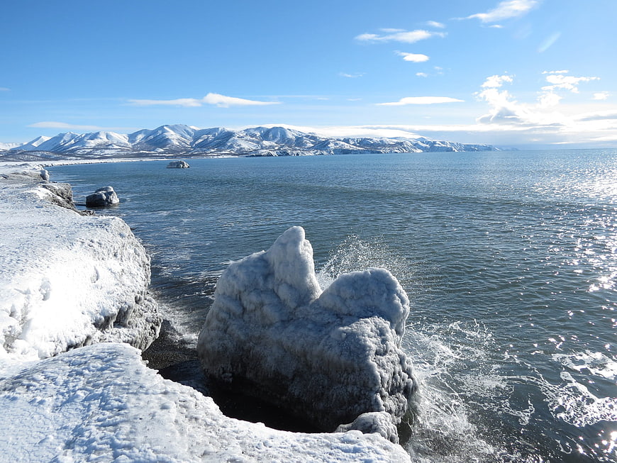 Frozen Rocks on Snowy Coastline with Mountain View